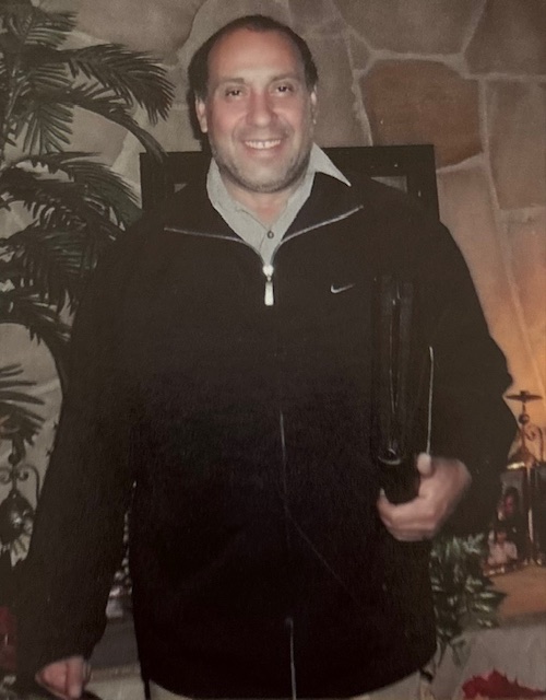 Portrait of Robert's father smiling, wearing a dark zip-up jacket